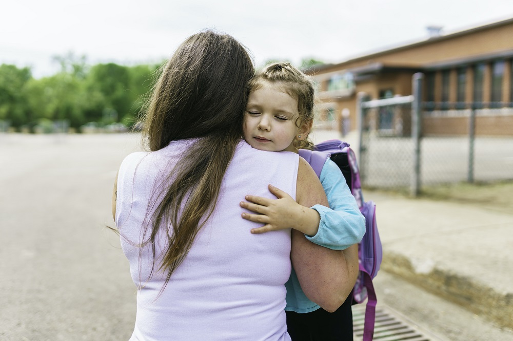 Mum hugging young girl outside school