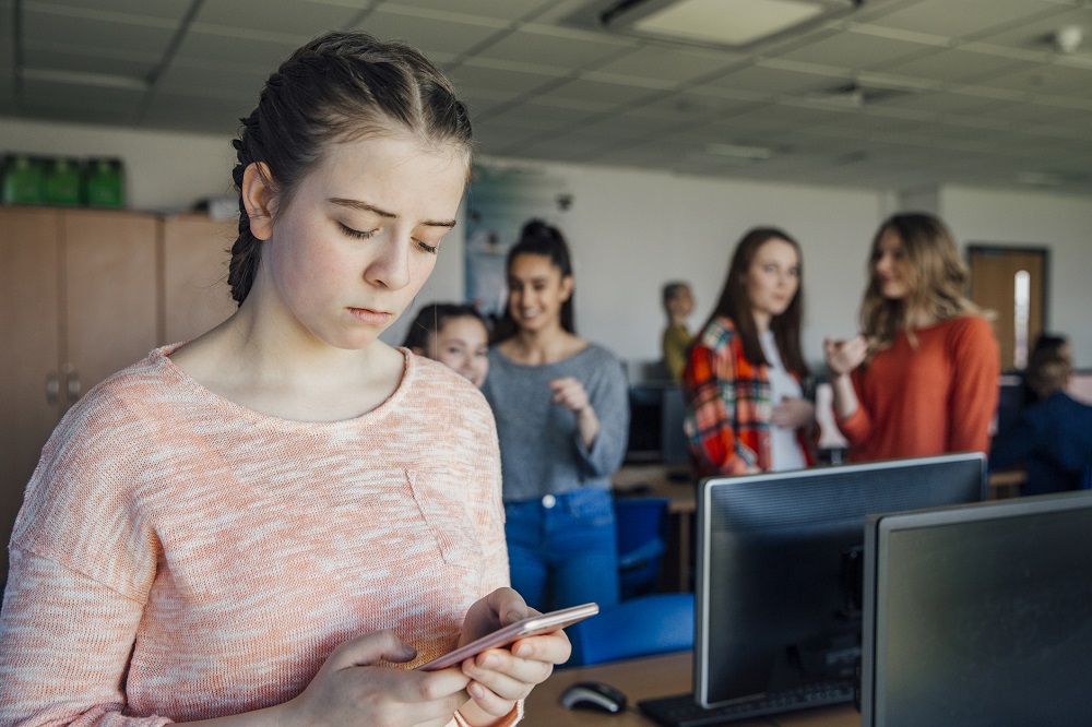 Sad teenage girl being left out by her friends in a classroom