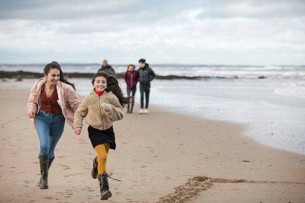 A family outing to the beach, with a teen girl running with her mum