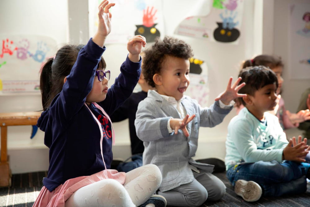 Image of children sitting in a playroom, waving their hands.