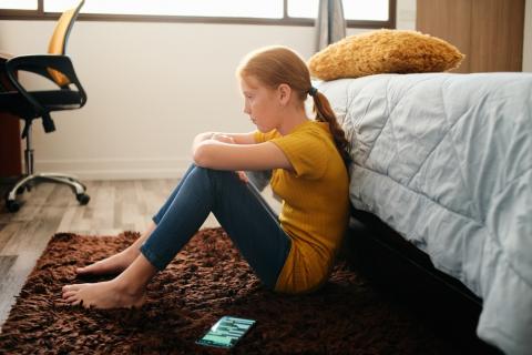 Sad teen girl in her bedroom, her mobile phone on the floor next to her